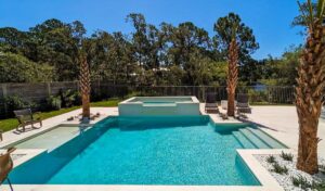 Luxury backyard pool with spa and palm trees under a clear blue sky.